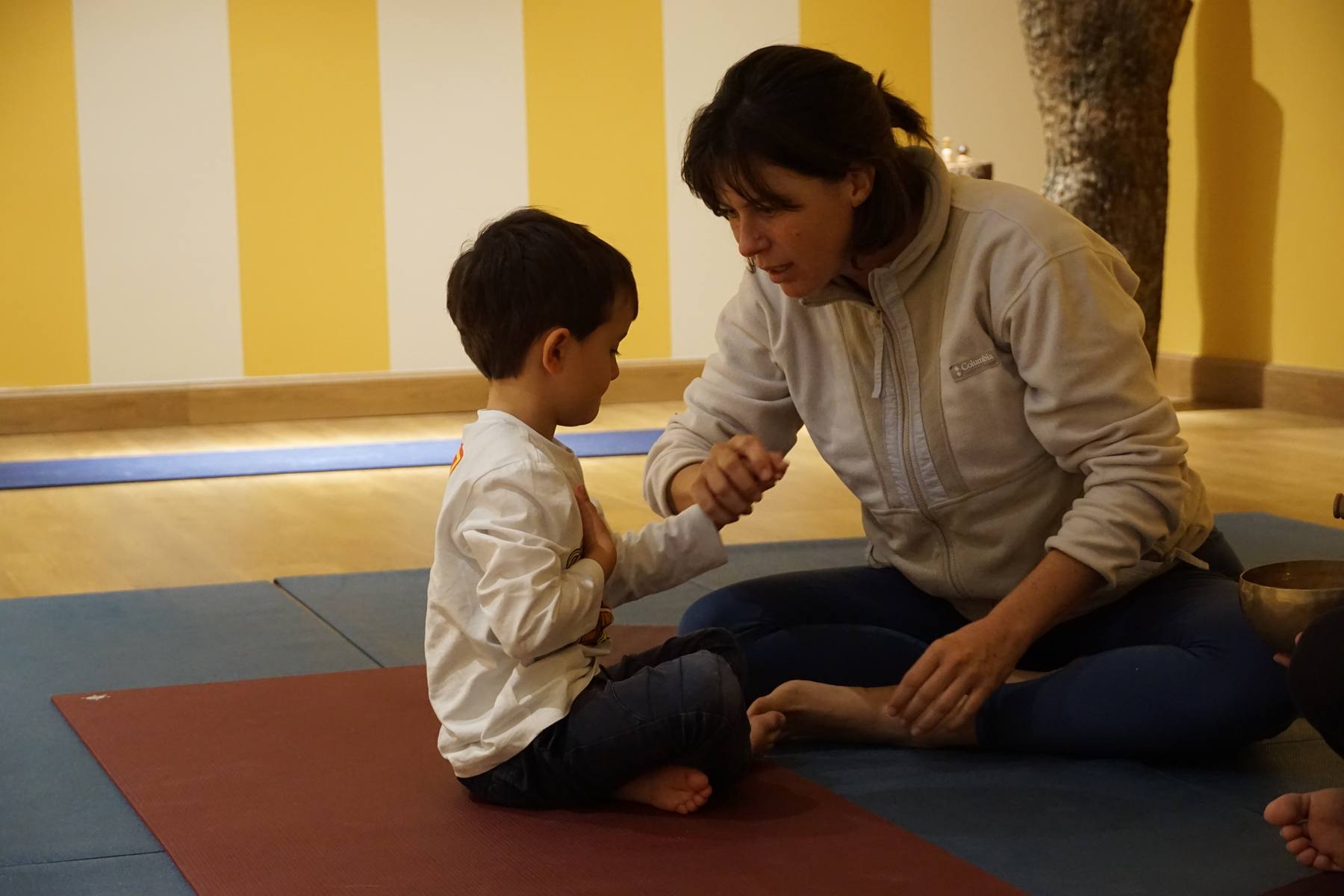 Francesca sitting face to face with a young child on a yoga mat, gently connecting during a session